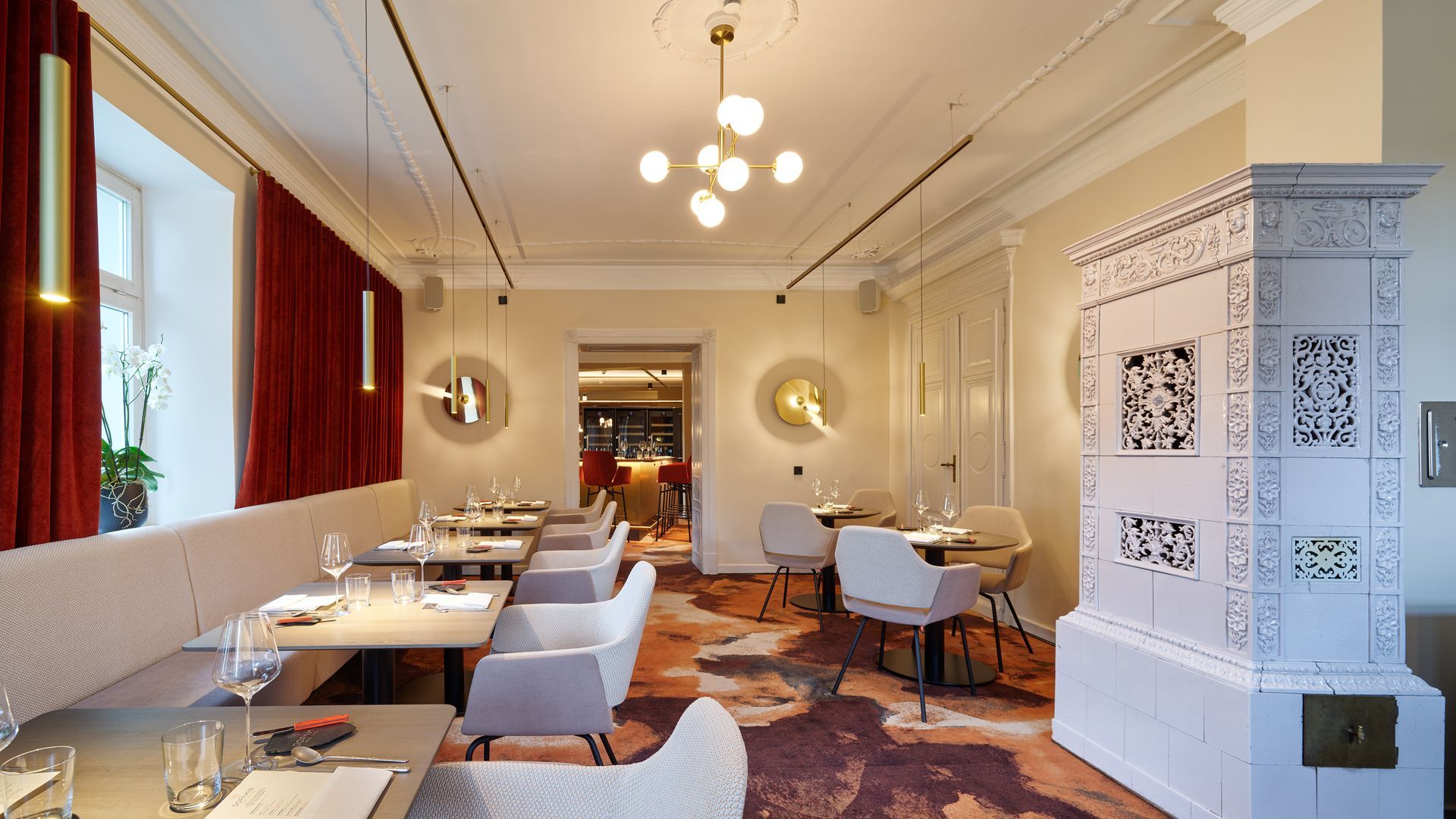 Eleganter Speisesaal mit weißen Tischen, gepolsterten Stühlen, roten Vorhängen und kunstvoller Wanddekoration