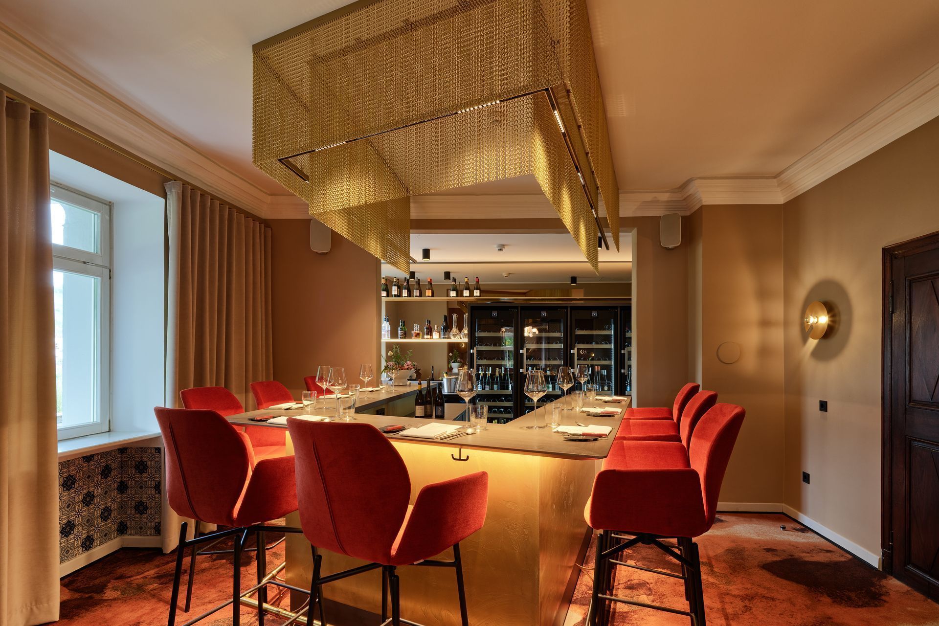 Elegantes Esszimmer mit roten Stühlen, langem Holztisch, Kronleuchter und Barbereich im Hintergrund