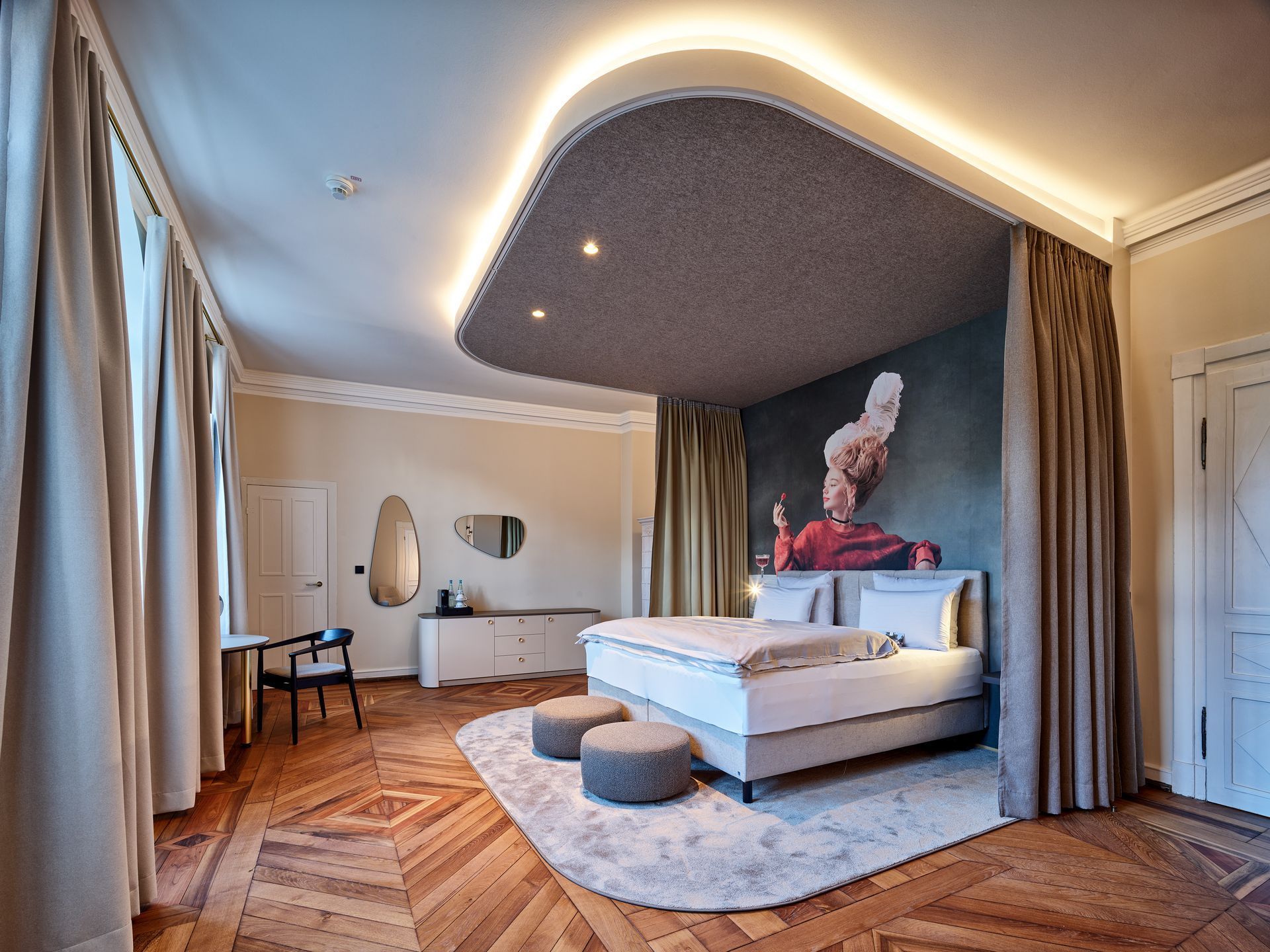 Modernes Schlafzimmer mit Kingsize-Bett, geschwungenen Deckenleuchten, großen Fenstern und einem weißen Teppich.
