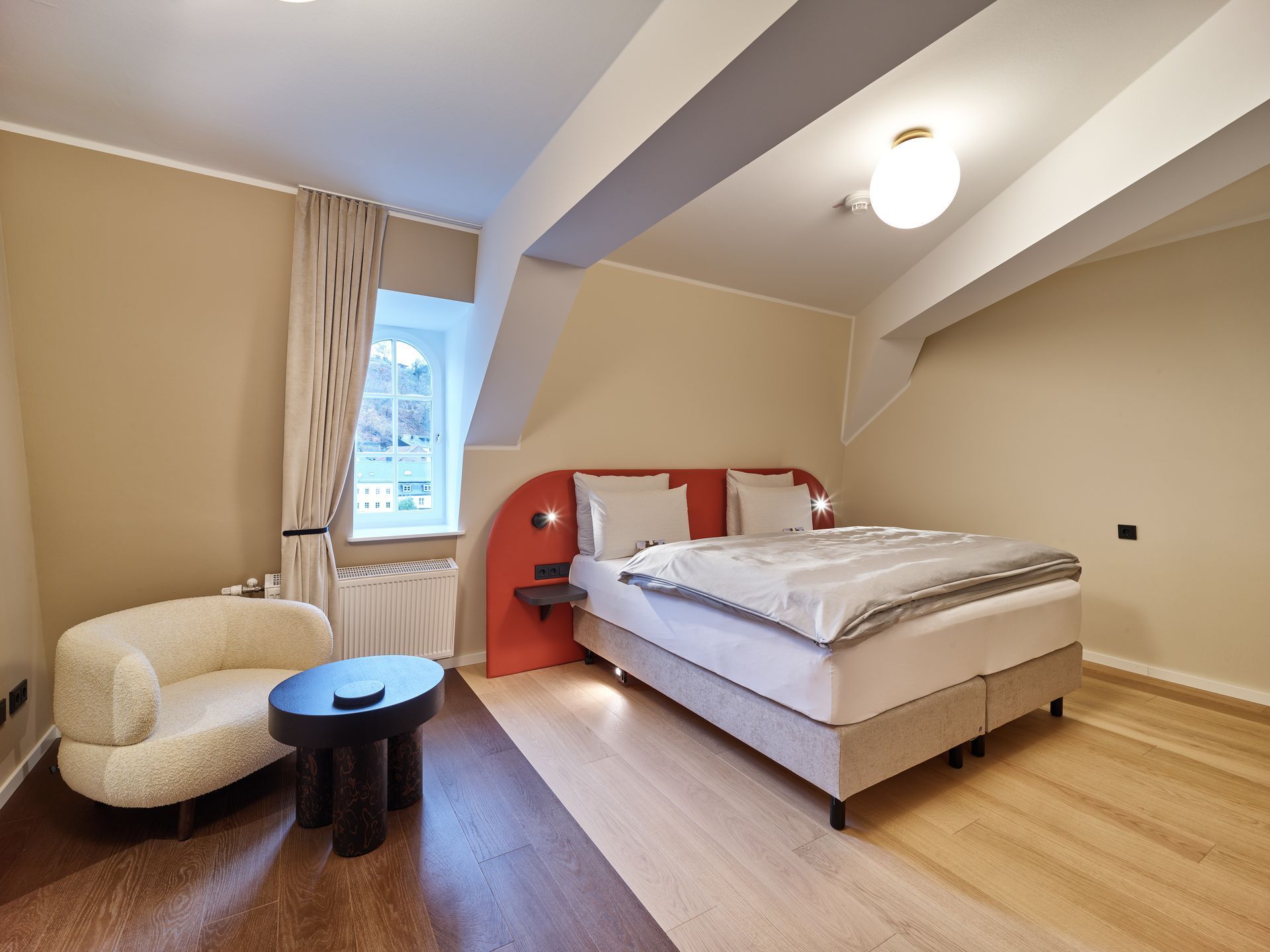 Modernes Schlafzimmer mit Kingsize-Bett, beigefarbenen Wänden, Fensterbank und einem cremefarbenen Sessel
