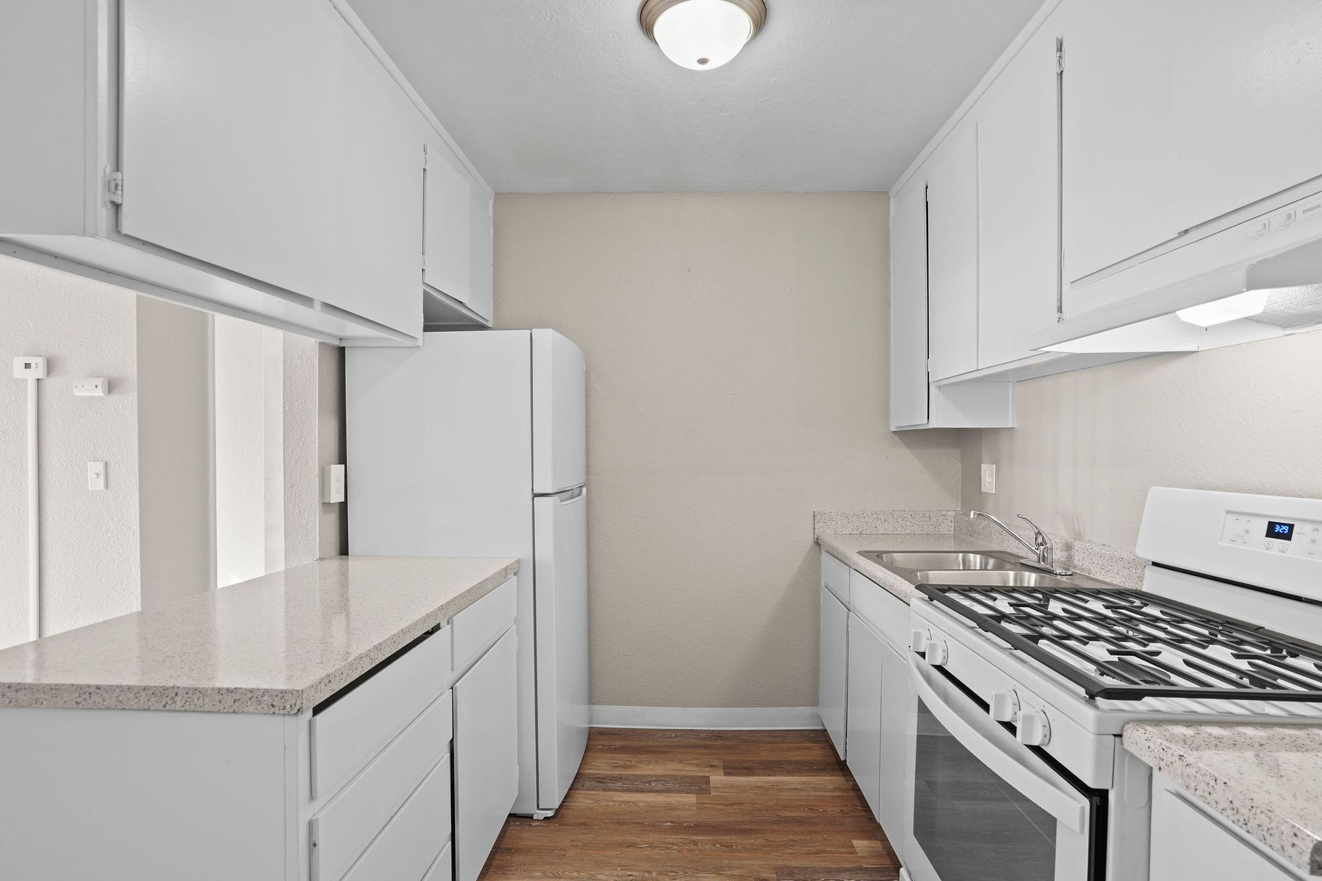 Narrow white kitchen with white cabinets, gray countertops, gas stove, and wood floor.