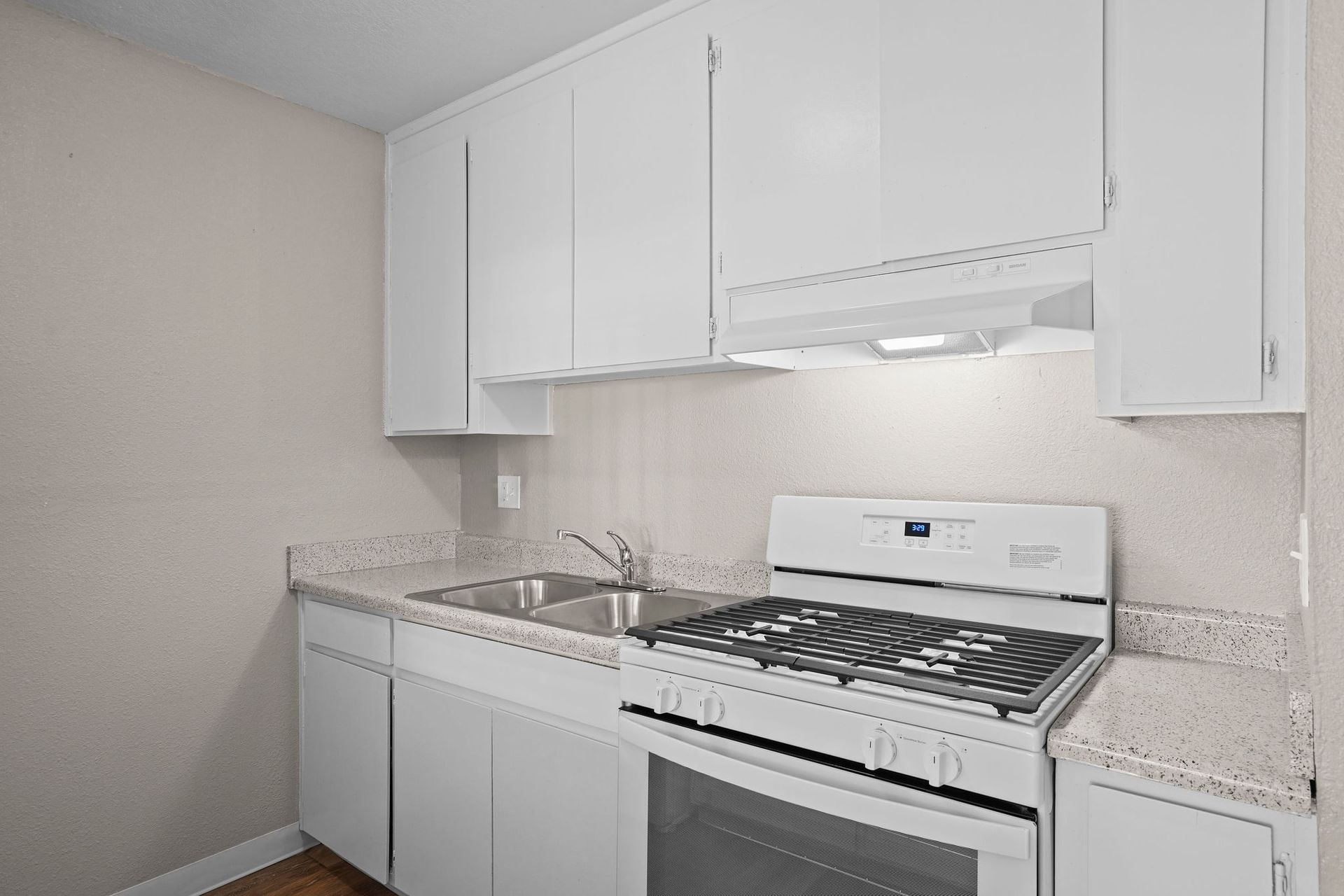 White kitchen with cabinets, granite countertop, sink, and white gas stove under a range hood.