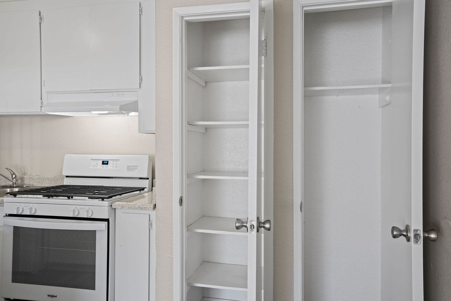 Small white kitchen with stove and two open pantry cabinets