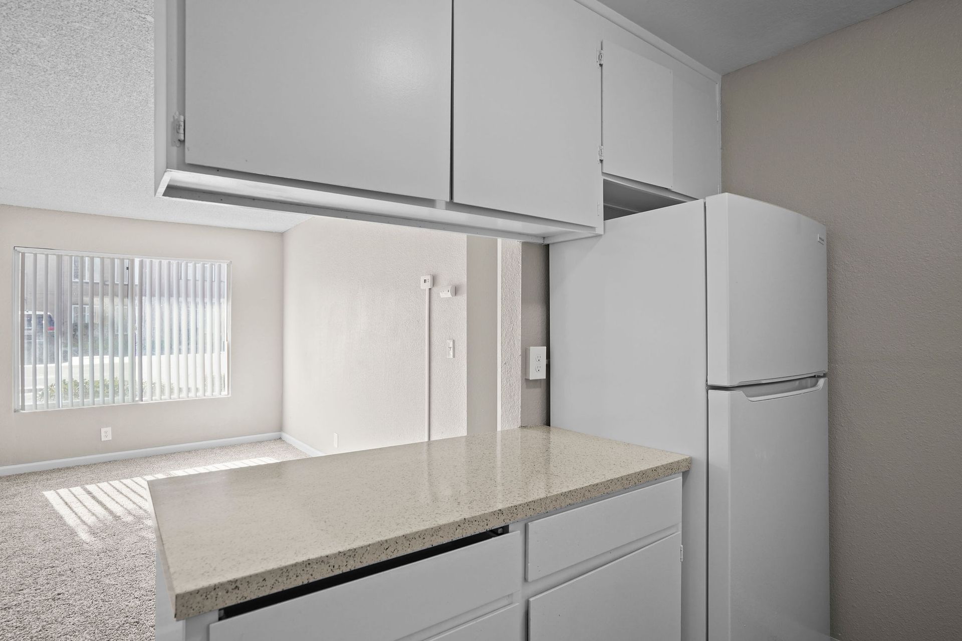 Small white kitchen with a countertop, upper cabinets, and a white refrigerator.