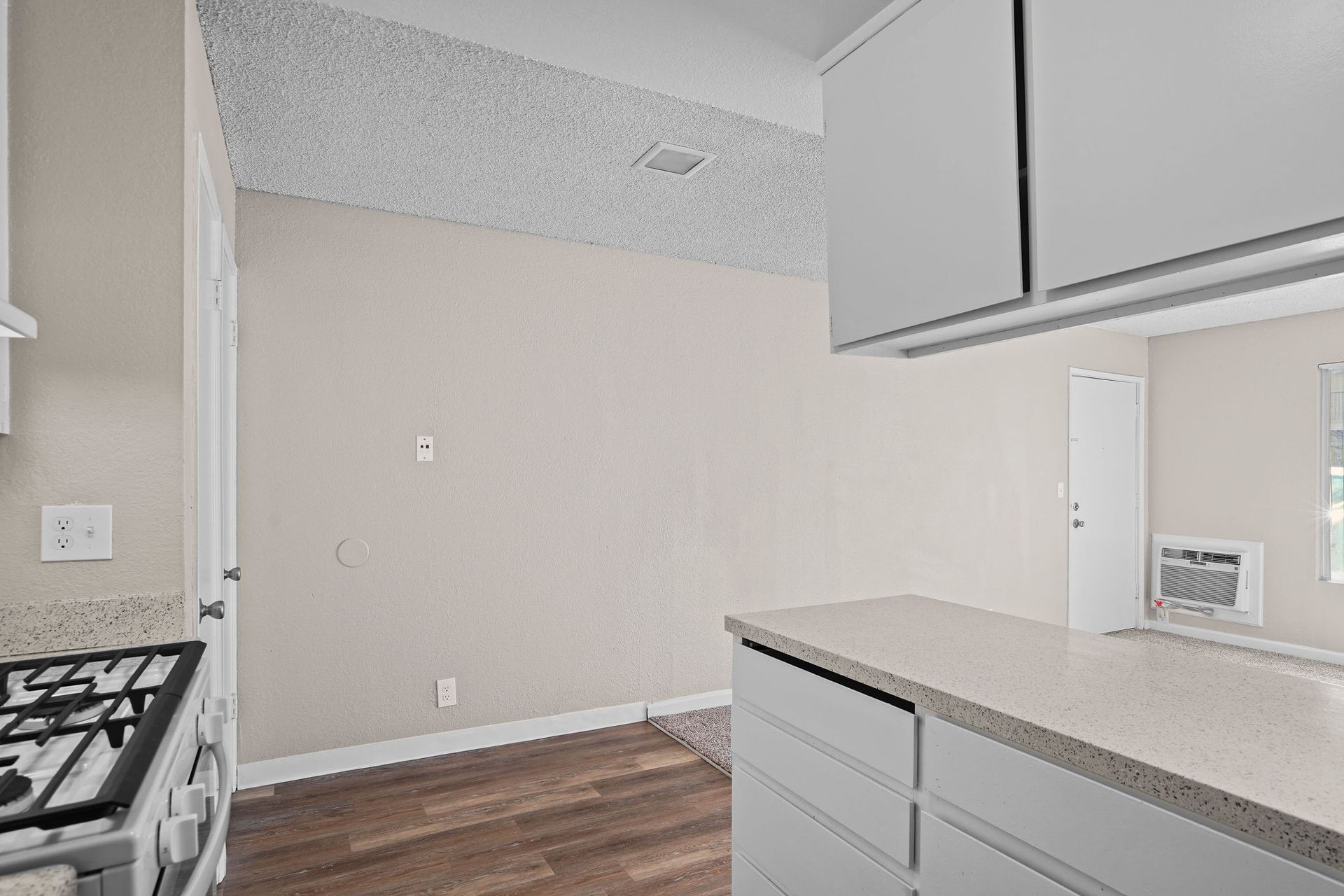 Empty kitchen with white cabinets, beige walls, and wood flooring