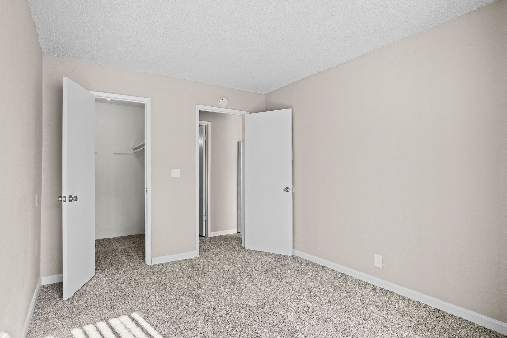 Empty beige bedroom with carpet, two open white doors, and a closet doorway.
