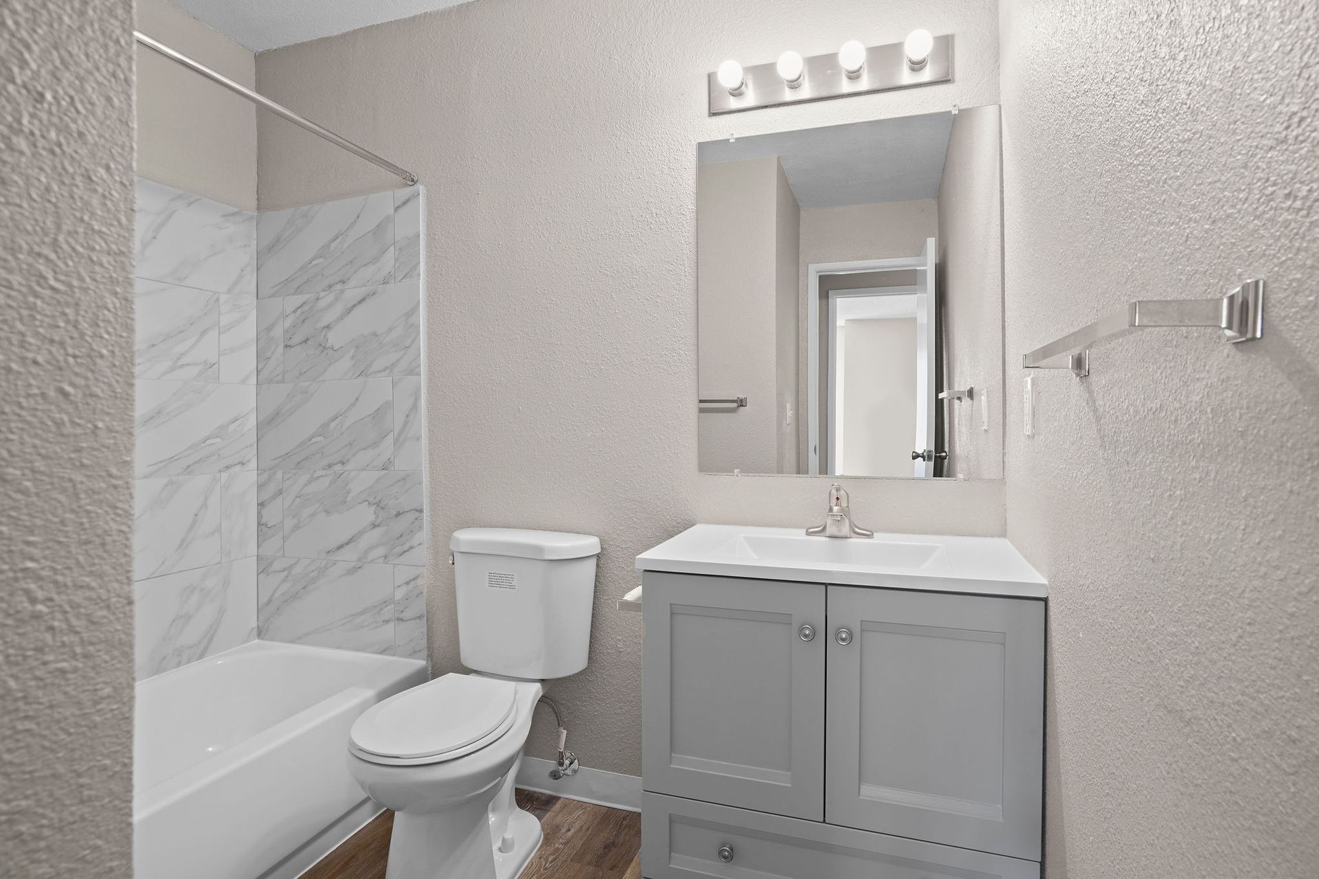 Small white bathroom with tub-shower, toilet, sink vanity, and mirror with lights.
