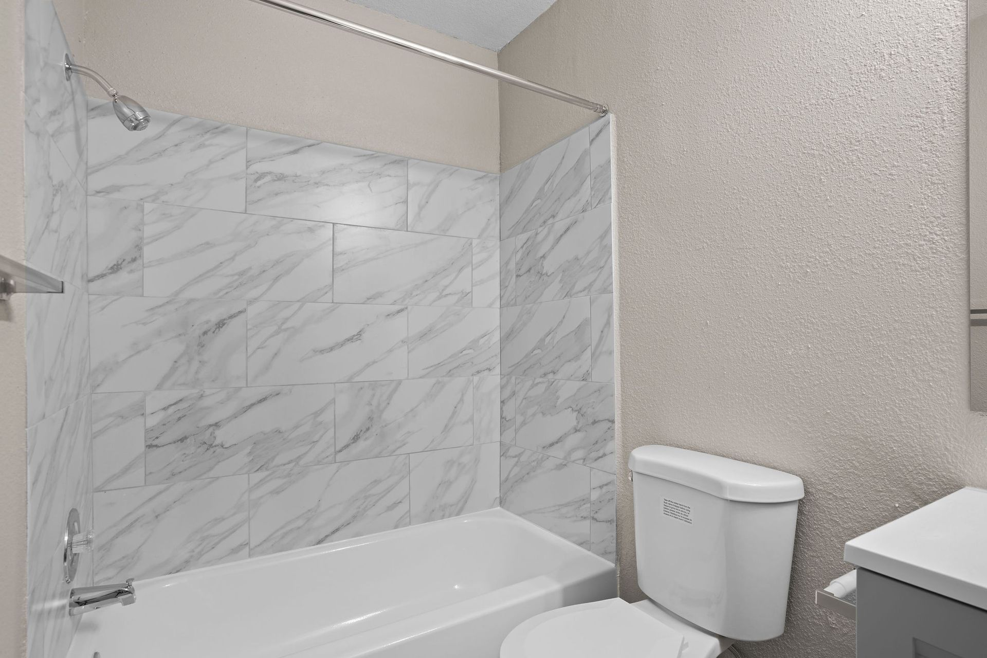 Modern bathroom with white marble shower walls, bathtub, toilet, and vanity sink