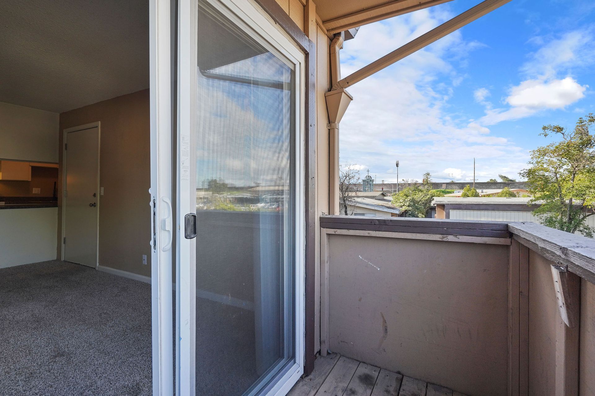 Small balcony with open door, beige railing, and a bright sky view.