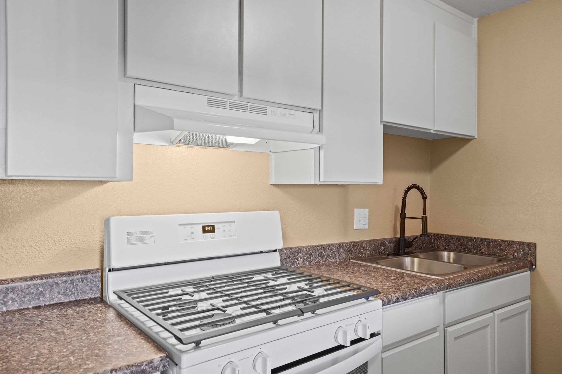 Compact kitchen with white cabinets, gas stove, granite counters, and a stainless sink.
