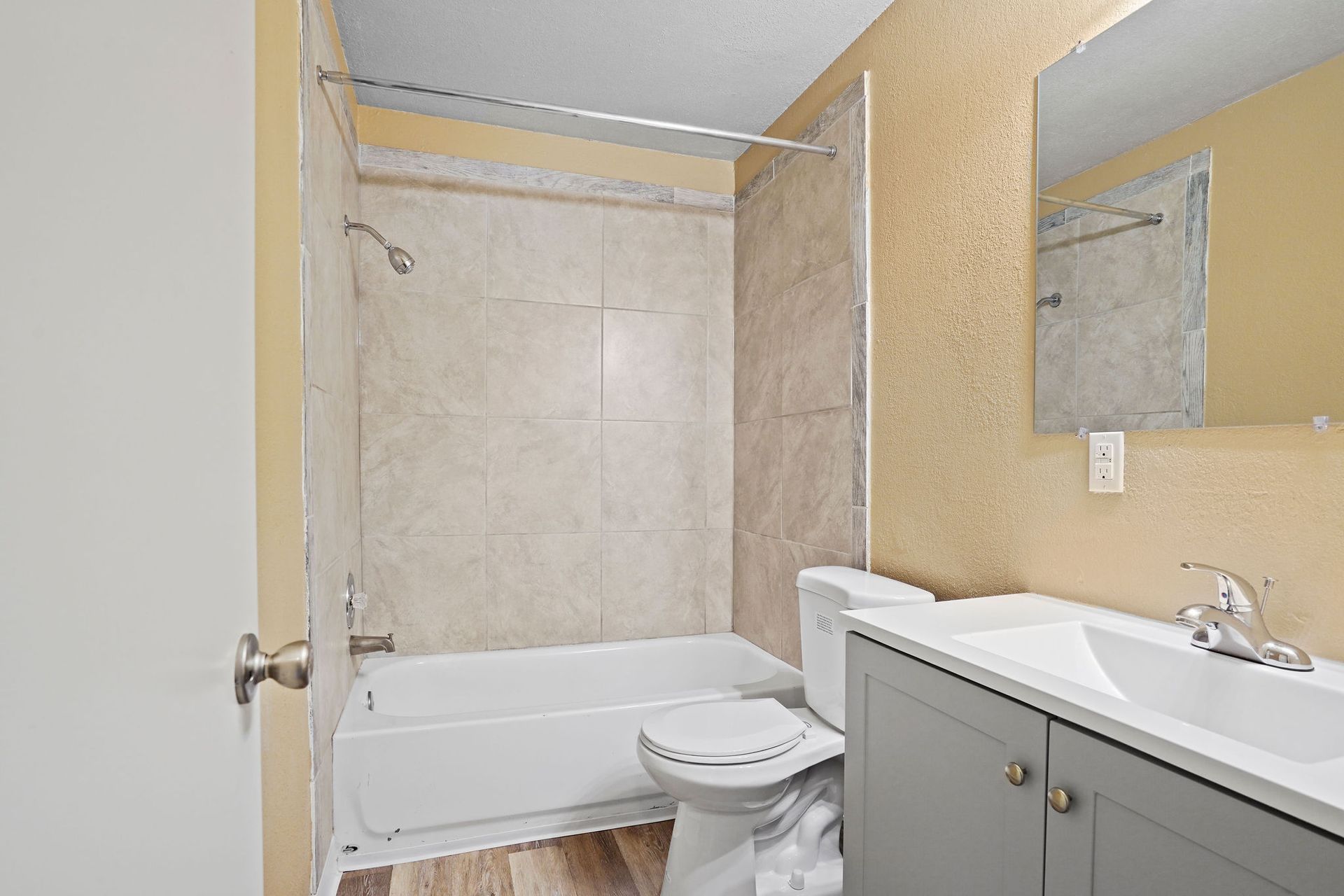 Small bathroom with a tub-shower, toilet, and white vanity with mirror.