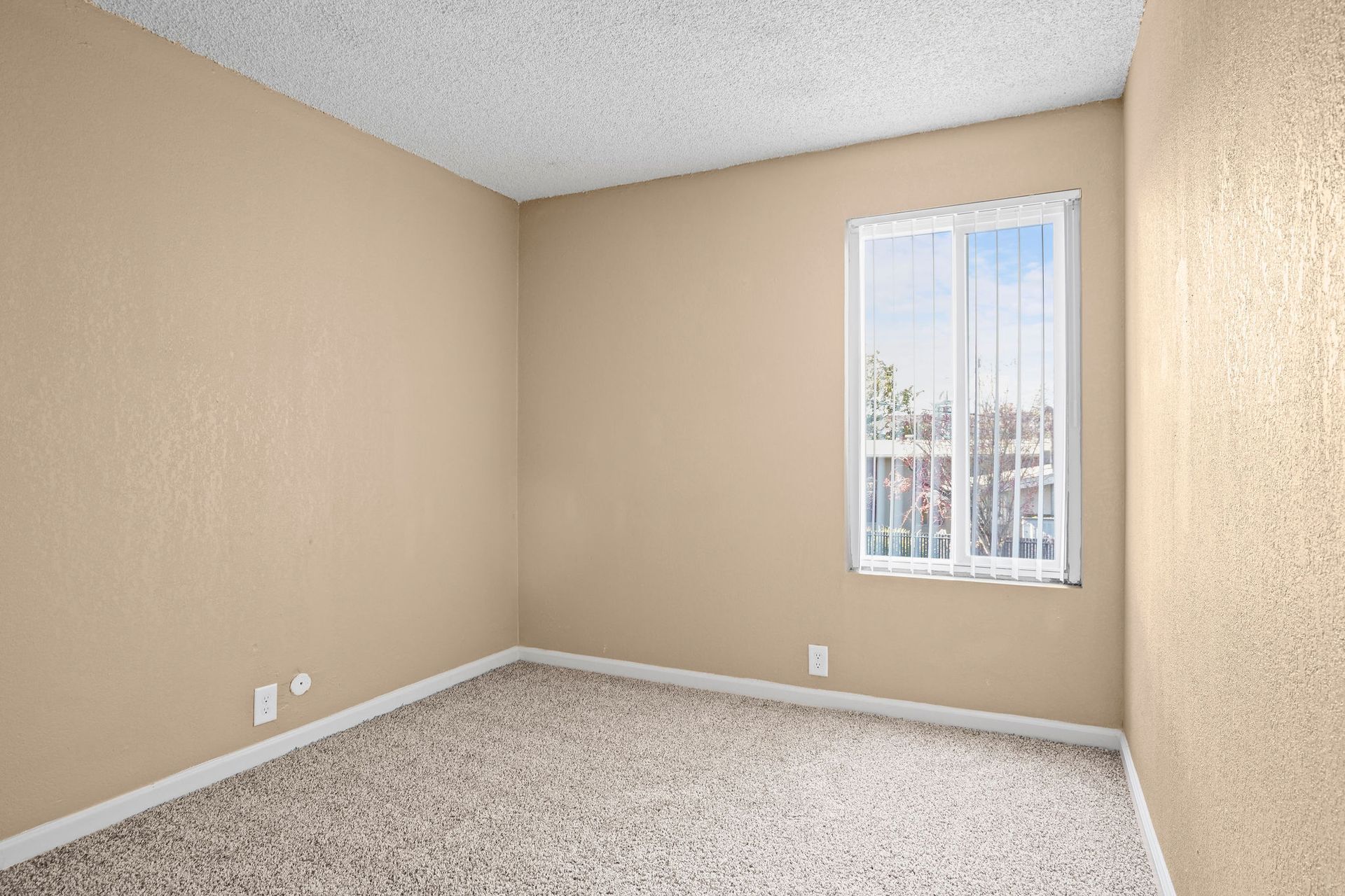 Empty beige bedroom with carpeted floor and a small window.