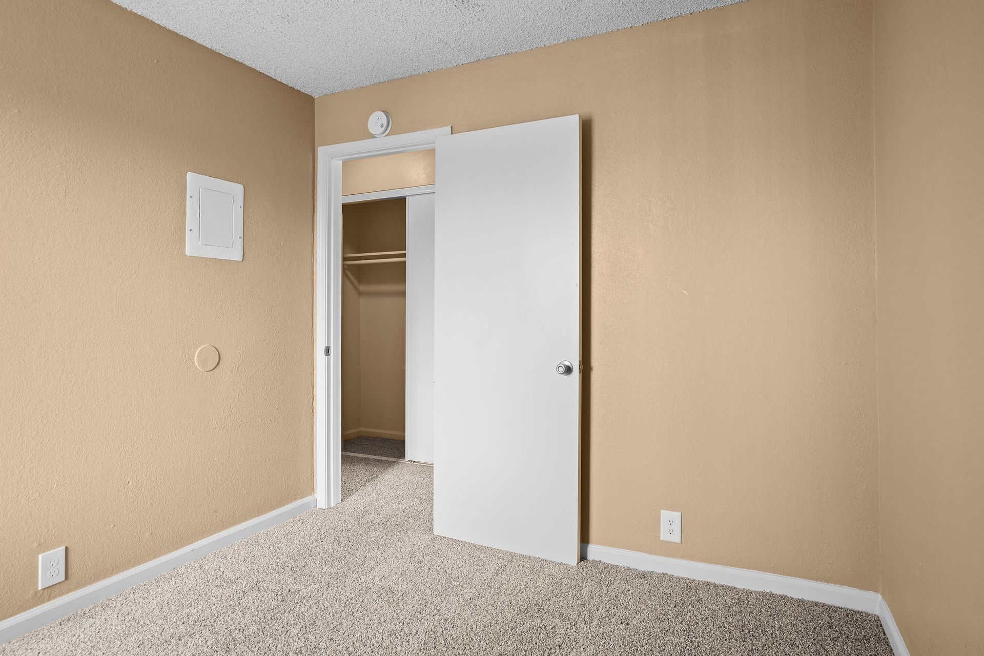Empty beige bedroom with open white closet door and carpeted floor