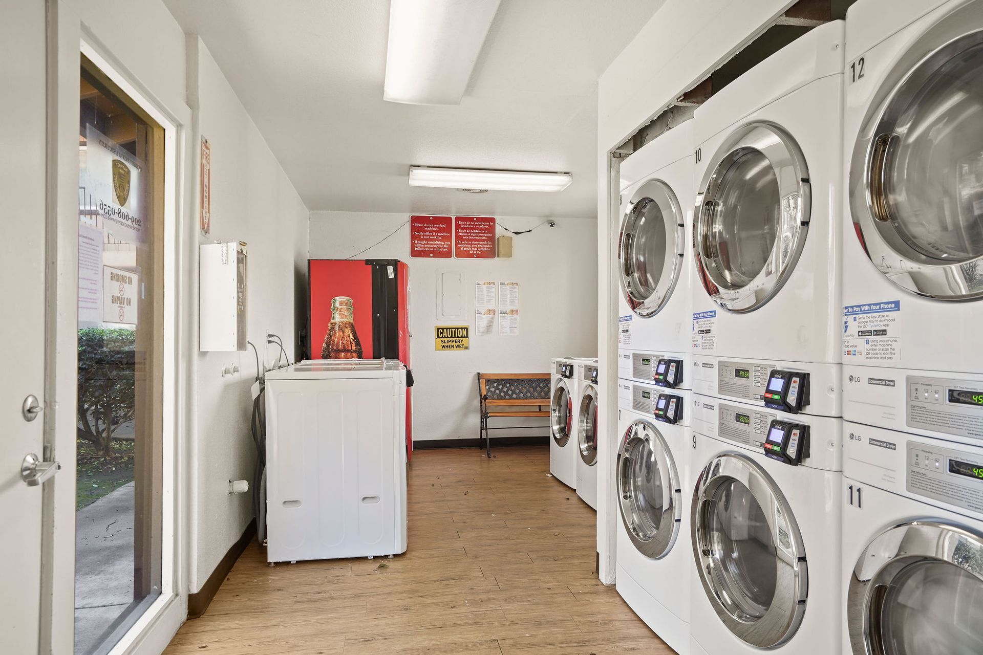 Bright laundromat with stacked washers and dryers, a washer in front, and open glass door to the left