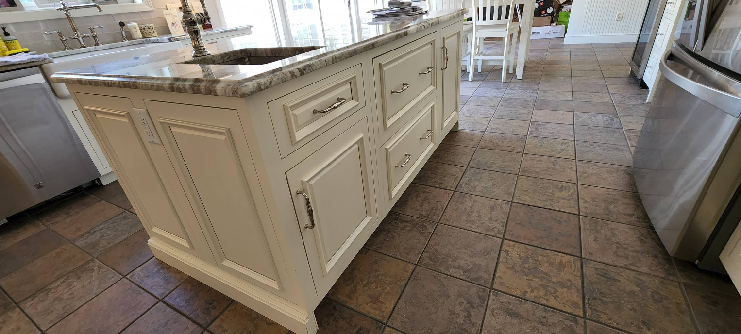 Kitchen island with white cabinets and marble countertop in a tiled kitchen floor, viewed at an angle