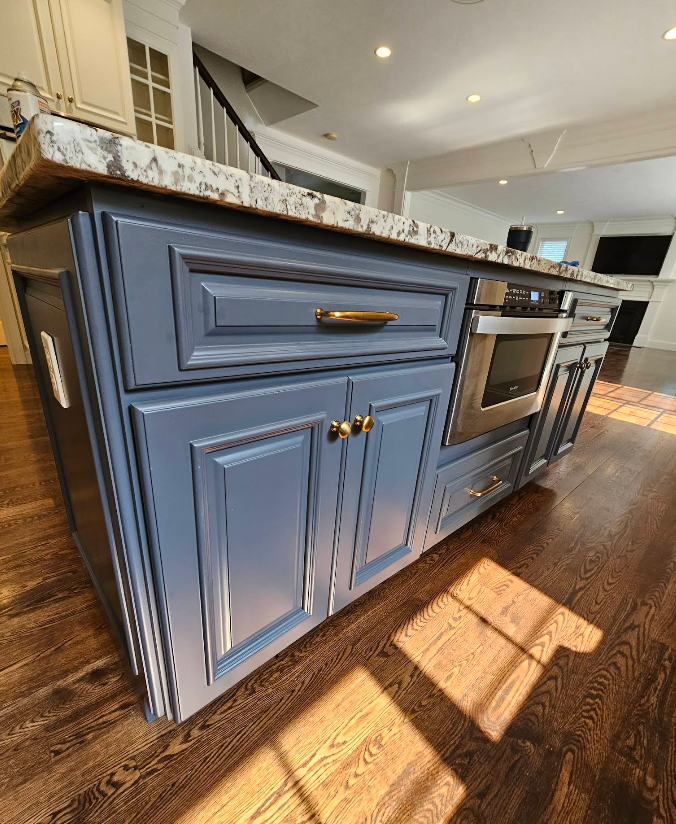 Blue kitchen island with marble countertop, brass handles, and built-in oven in a sunlit room