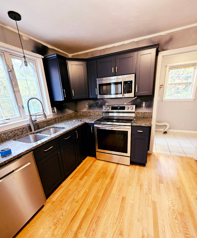 Modern kitchen with dark cabinets, stainless appliances, granite counters, and light wood floors.