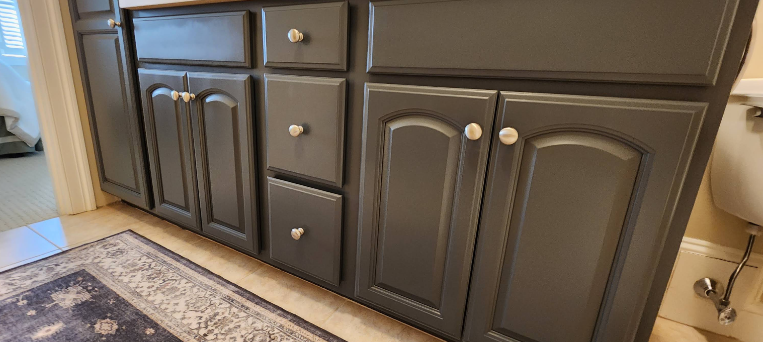 Dark wood bathroom vanity with cabinet doors and drawers beside a rug and tiled floor.