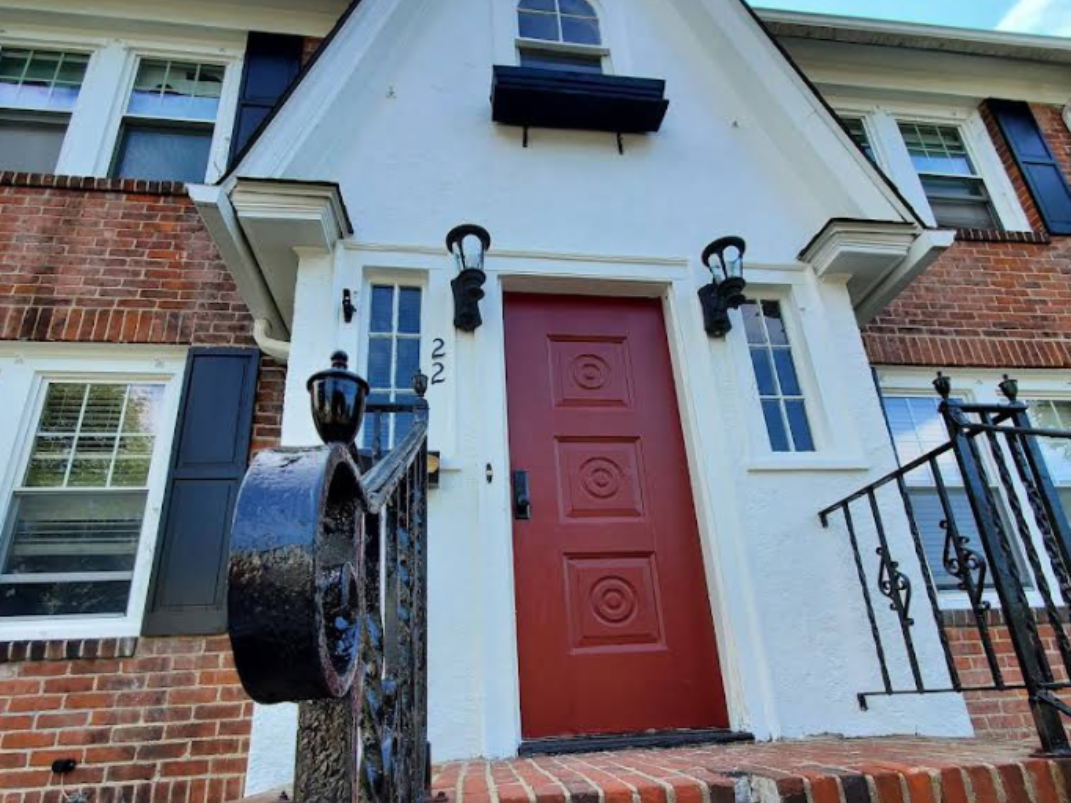Front entrance of a brick building with a red door, black mailbox, and blue-trimmed windows.