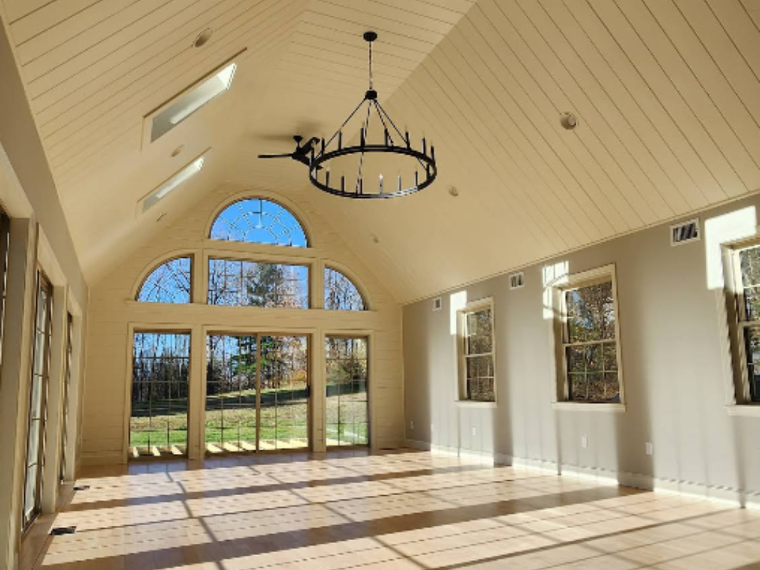 Bright, empty hall with arched windows, white walls, and a chandelier under a vaulted ceiling.