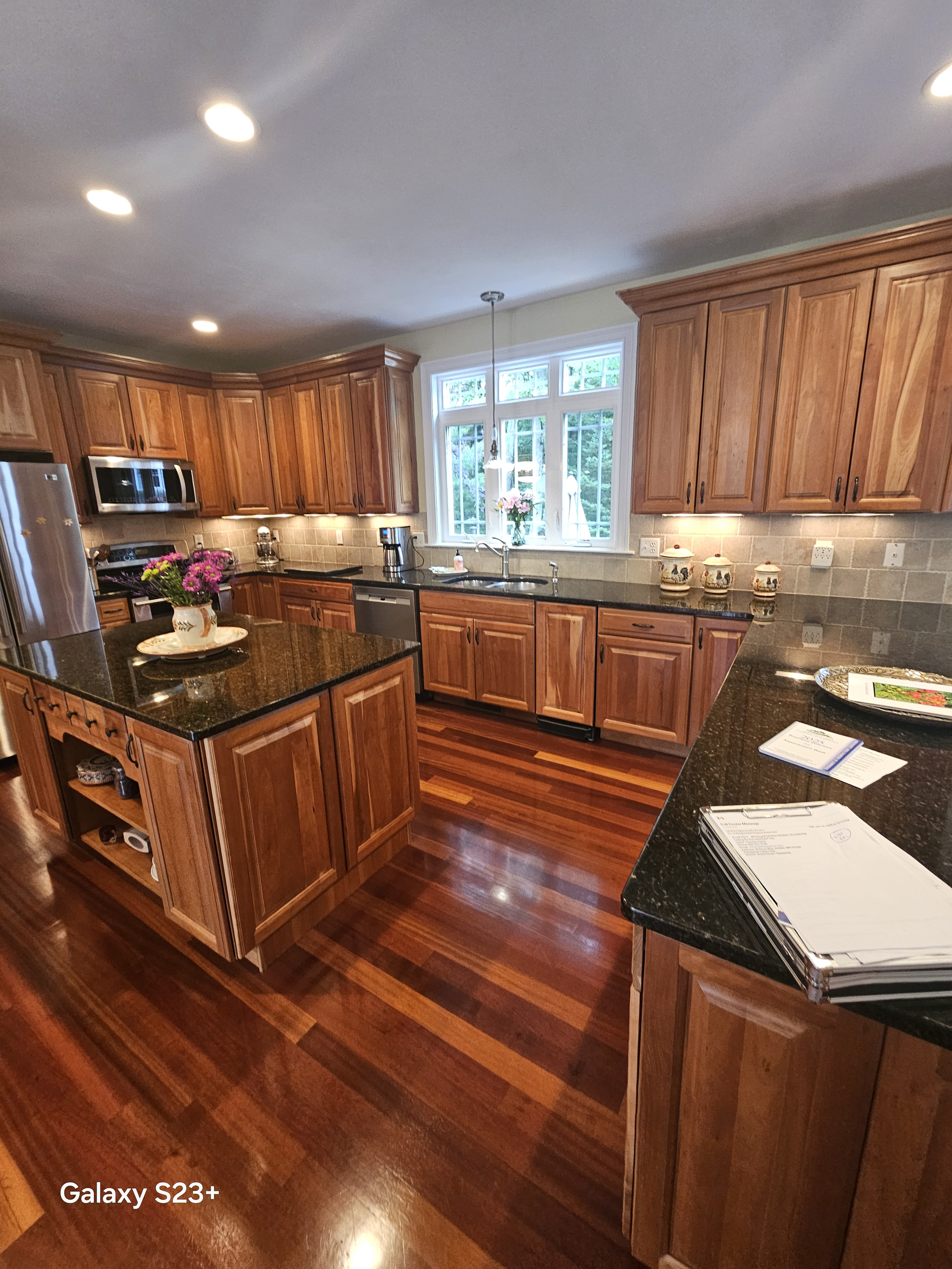 Bright kitchen with wood cabinets, dark countertops, and a central island on polished hardwood floors.