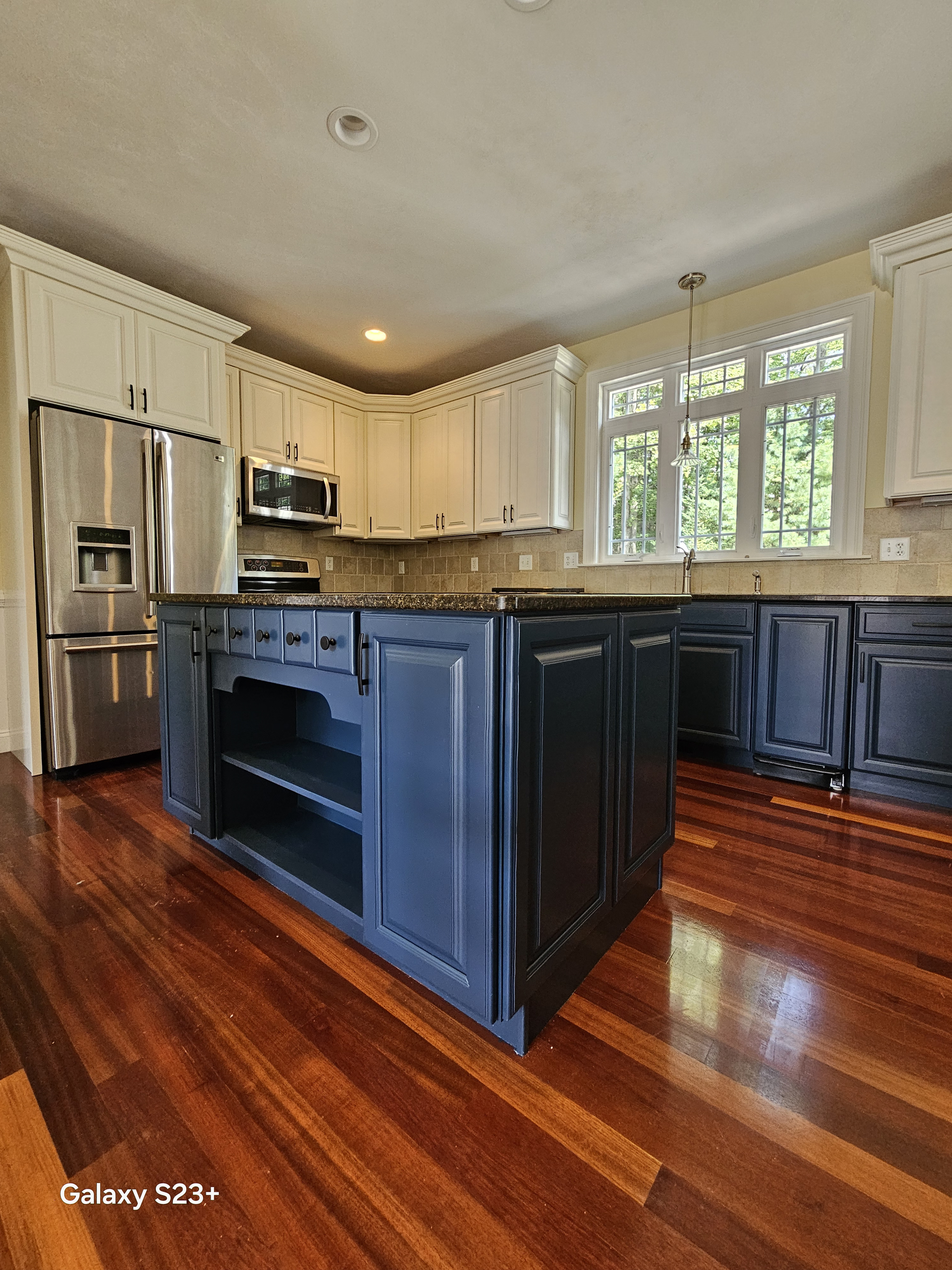 Bright kitchen with dark island, white cabinets, stainless fridge, and hardwood floors