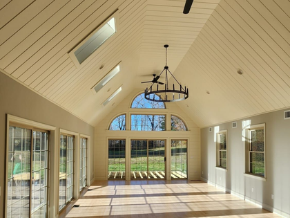Bright sunroom with vaulted ceiling, skylights, chandelier, and large glass doors overlooking a lawn.