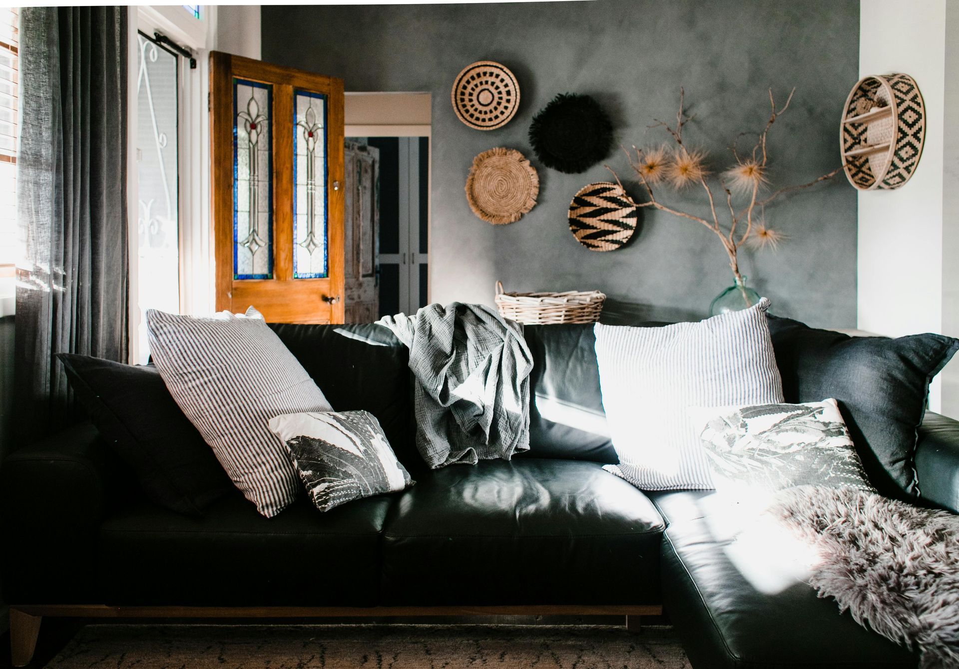 A living room with a black leather couch and wicker baskets on the wall.