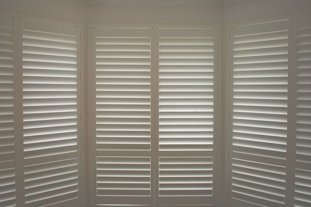 A Window With White Shutters on It in a Room — Curtain Haven & Blinds in Laurieton, NSW