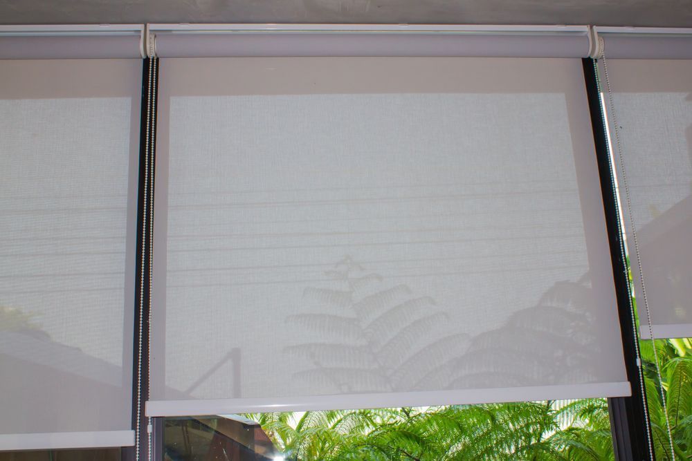 A Close Up of a Window With White Roller Blinds on It — Curtain Haven & Blinds in Laurieton, NSW