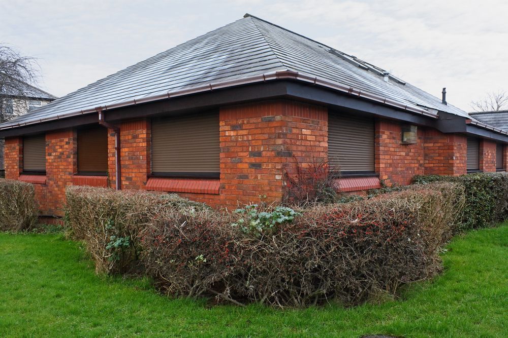 A Brick Building With a Roof and a Few Bushes in Front of It — Curtain Haven & Blinds in Lake Cathie, NSW