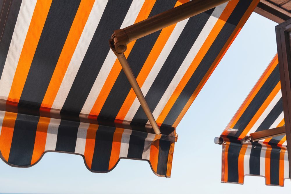 A Black and Orange Striped Awning Against a Blue Sky — Curtain Haven & Blinds in Harrington, NSW