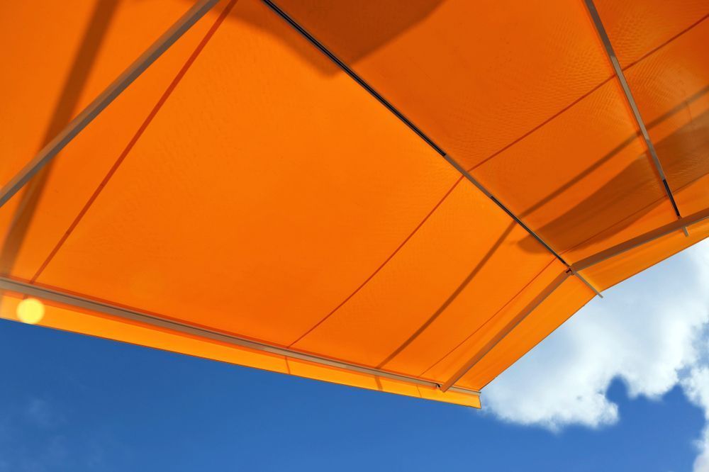 An Orange Awning Against a Blue Sky With Clouds — Curtain Haven & Blinds in Wauchope, NSW