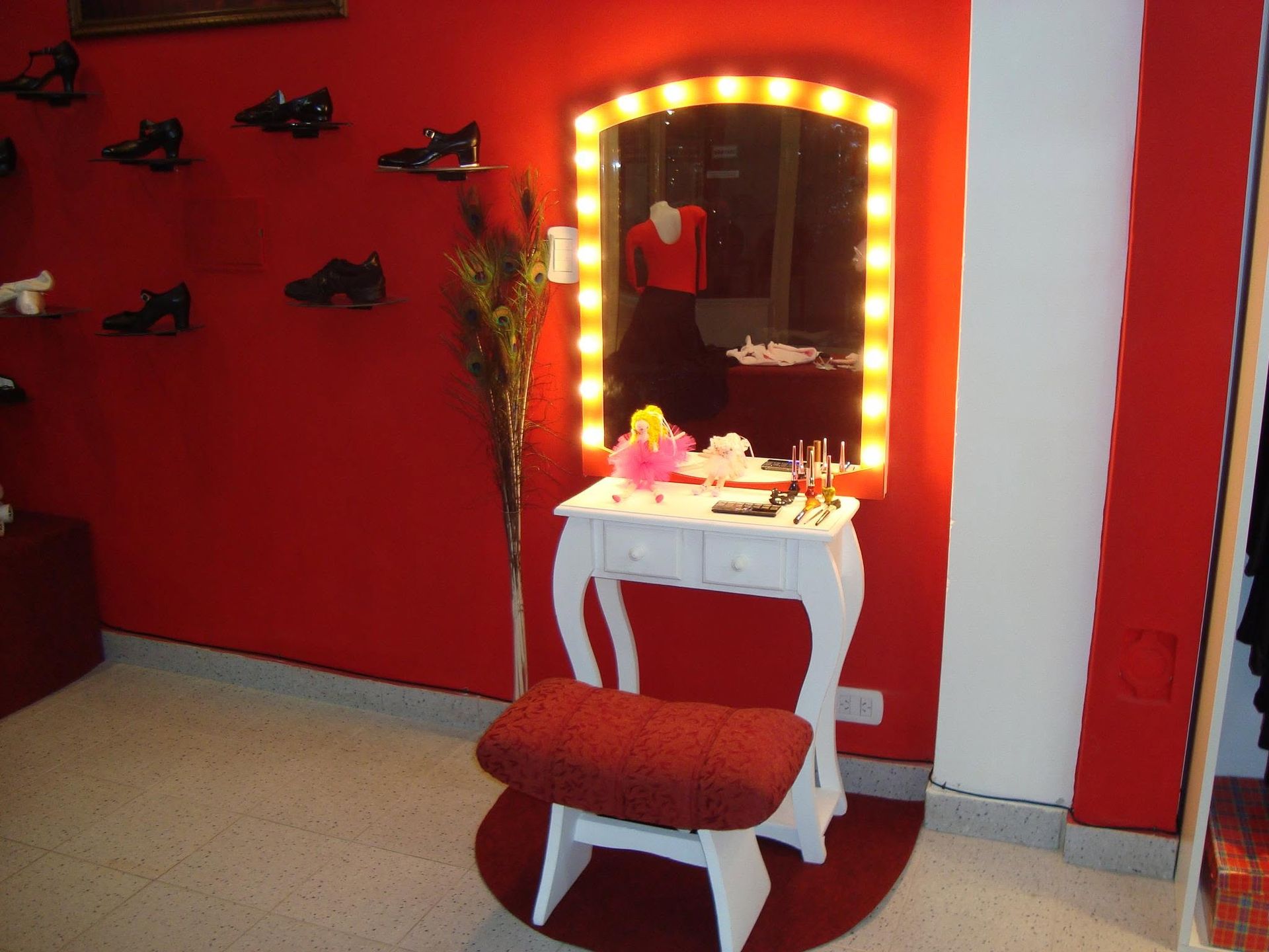 Vestidor con paredes rojas, espejo de tocador iluminado, mesa blanca y taburete rojo.