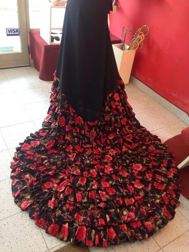 Vestido negro con cola de volantes rojos y negros, expuesto en un maniquí en el interior de un edificio.