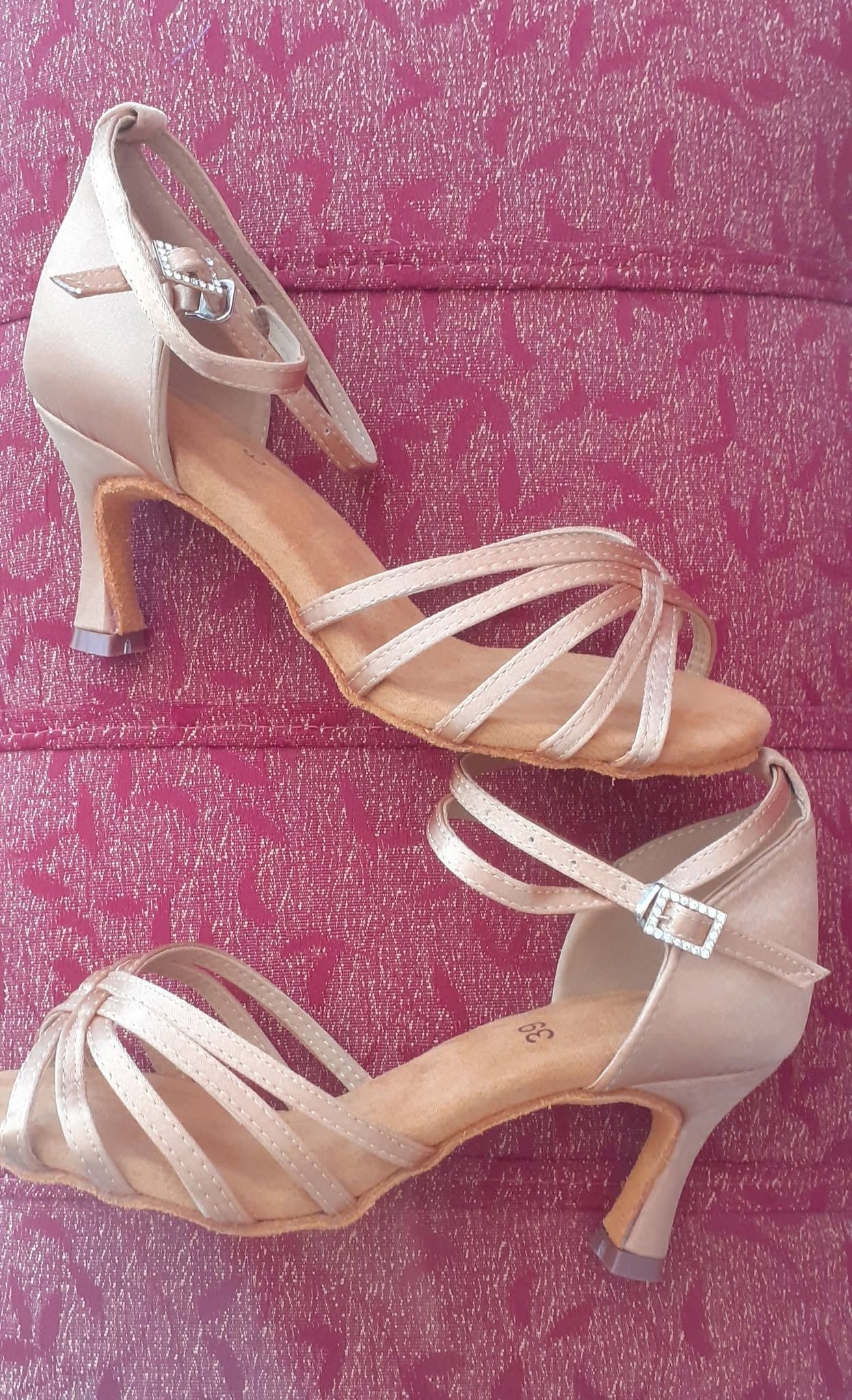 Un par de sandalias beige de tacón alto con tiras sobre un fondo rosa brillante.