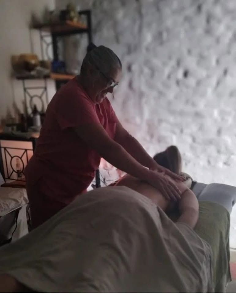Rosita Giordano con una camisa roja se inclina sobre una cama y le da un suave masaje a un paciente.