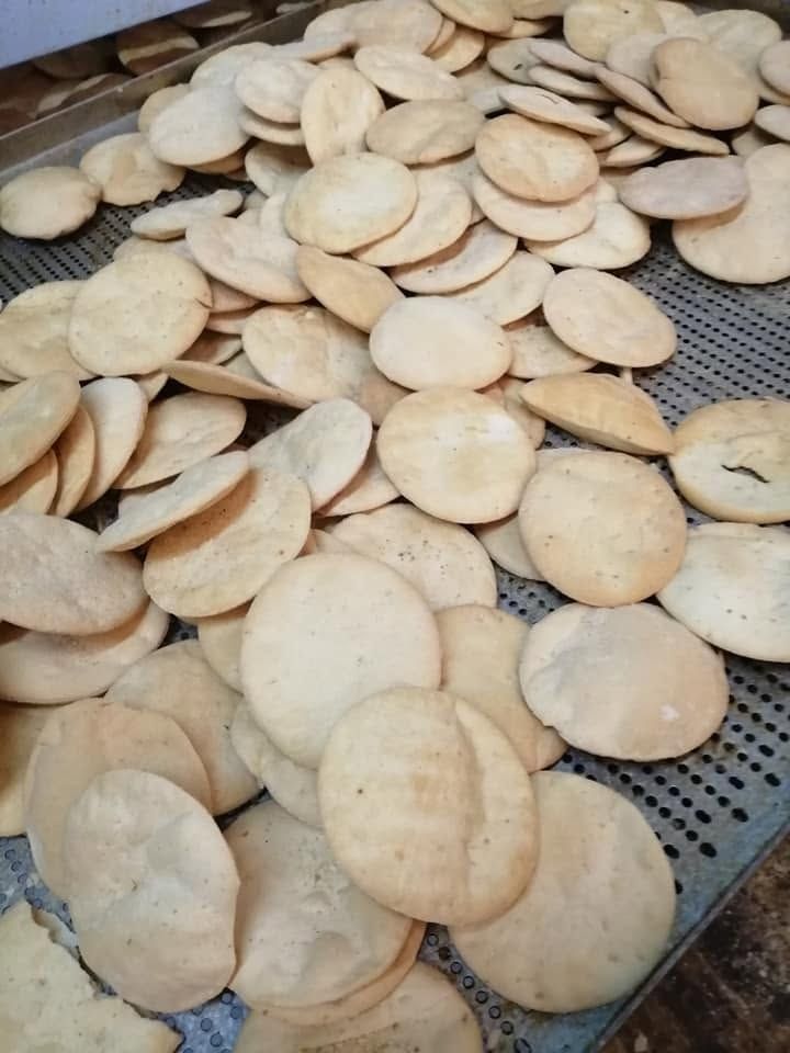 Montones de galletas o panes planos redondos y pálidos, horneados, enfriándose en bandejas de metal.