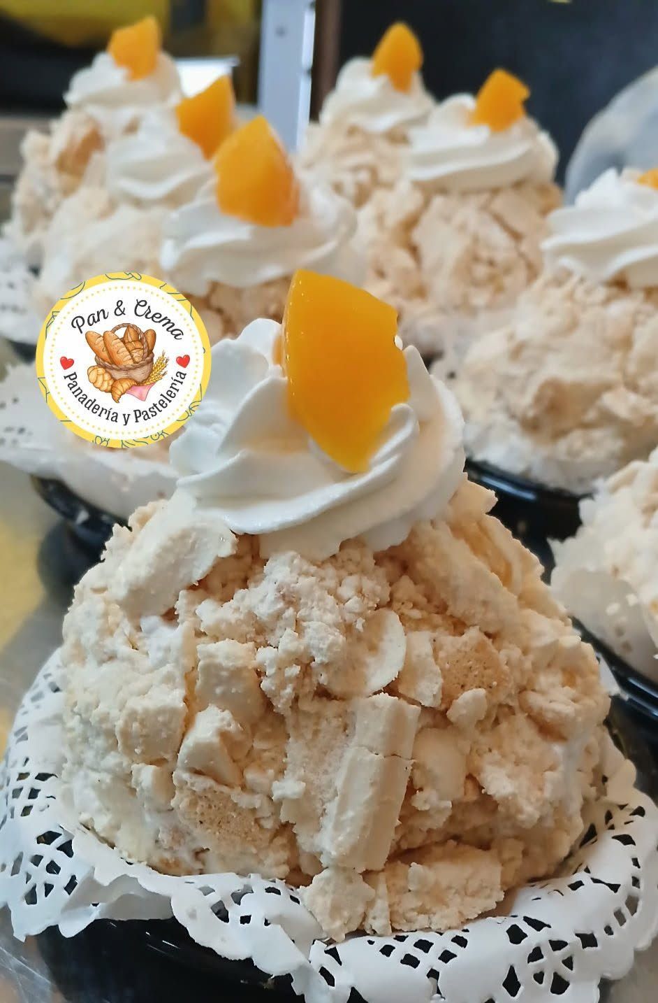 Mini pasteles de crema con cobertura de melocotón en bandejas negras, con glaseado batido y tapetes de encaje.