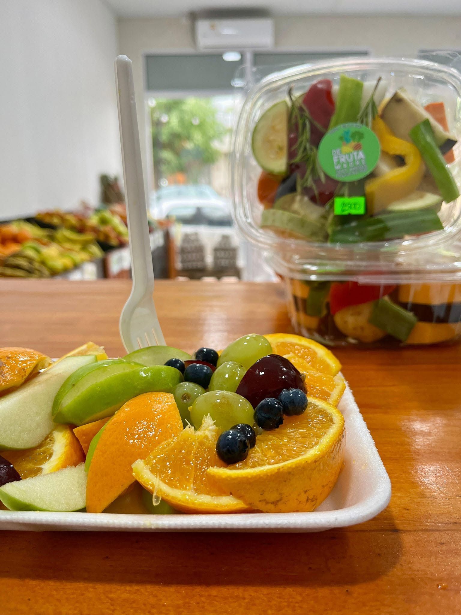 Plato de fruta fresca con rodajas de naranja, uvas y gajos de manzana junto a un vaso transparente con fruta variada.