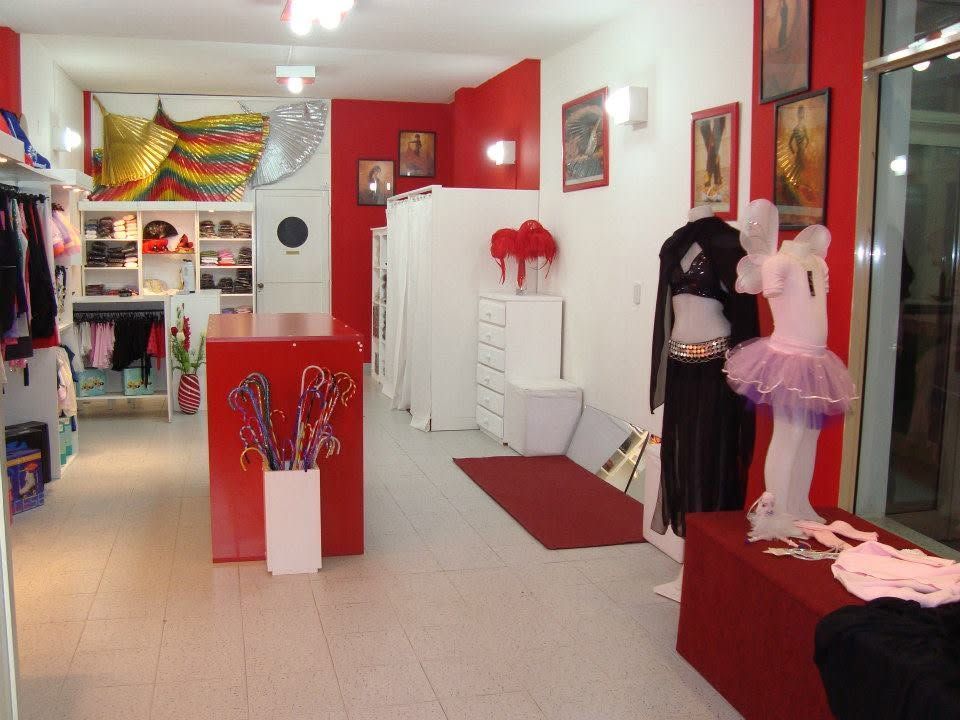 Interior de boutique con decoración en rojo y blanco, exhibidores de ropa y maniquíes cerca de la entrada.