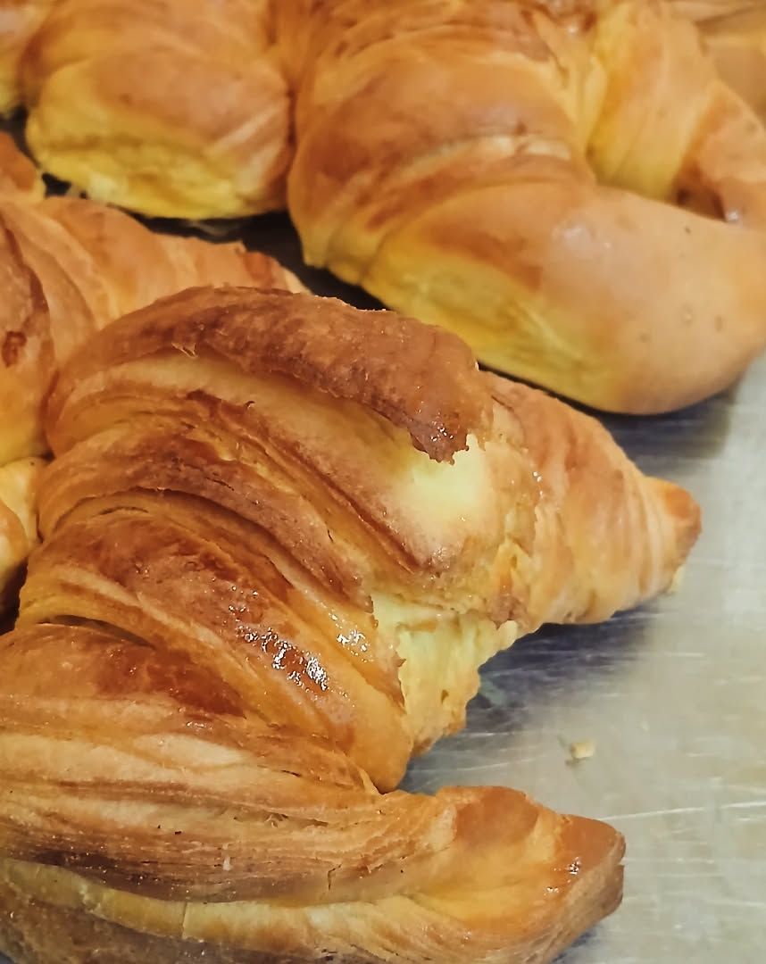 Croissants dorados en una bandeja para hornear, con capas hojaldradas y una corteza brillante.