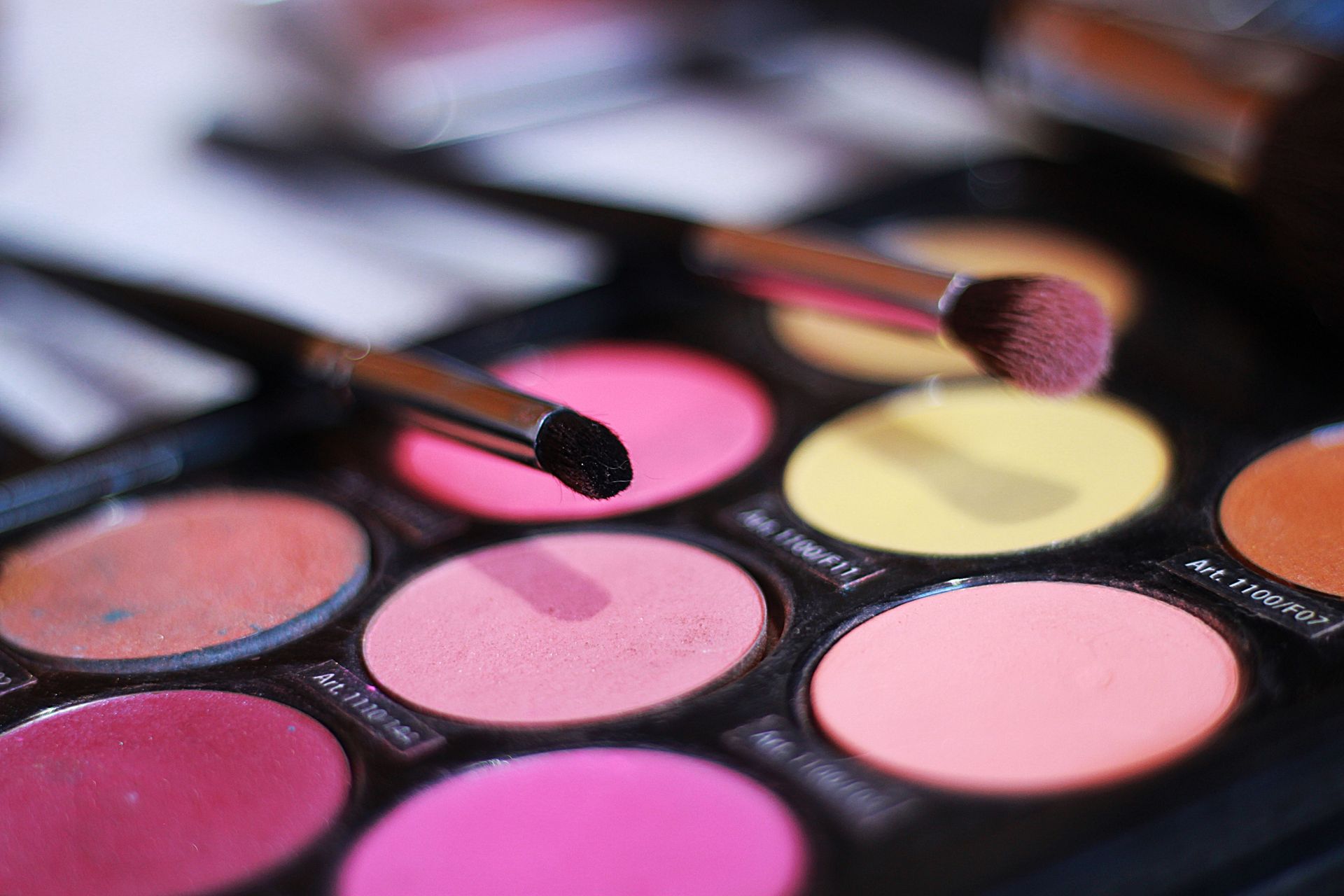 Paleta de sombras de ojos con tonos rosa y amarillo y dos pinceles.