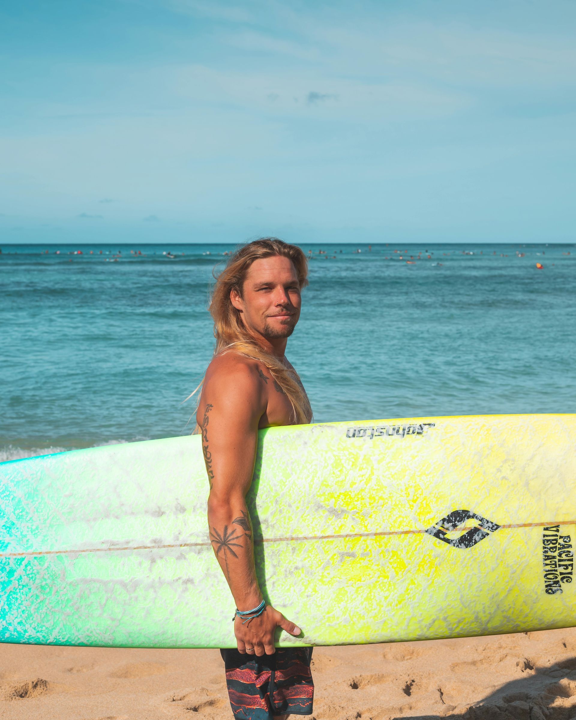 Una persona sostiene una tabla de surf amarilla en una playa de arena con el océano de fondo.