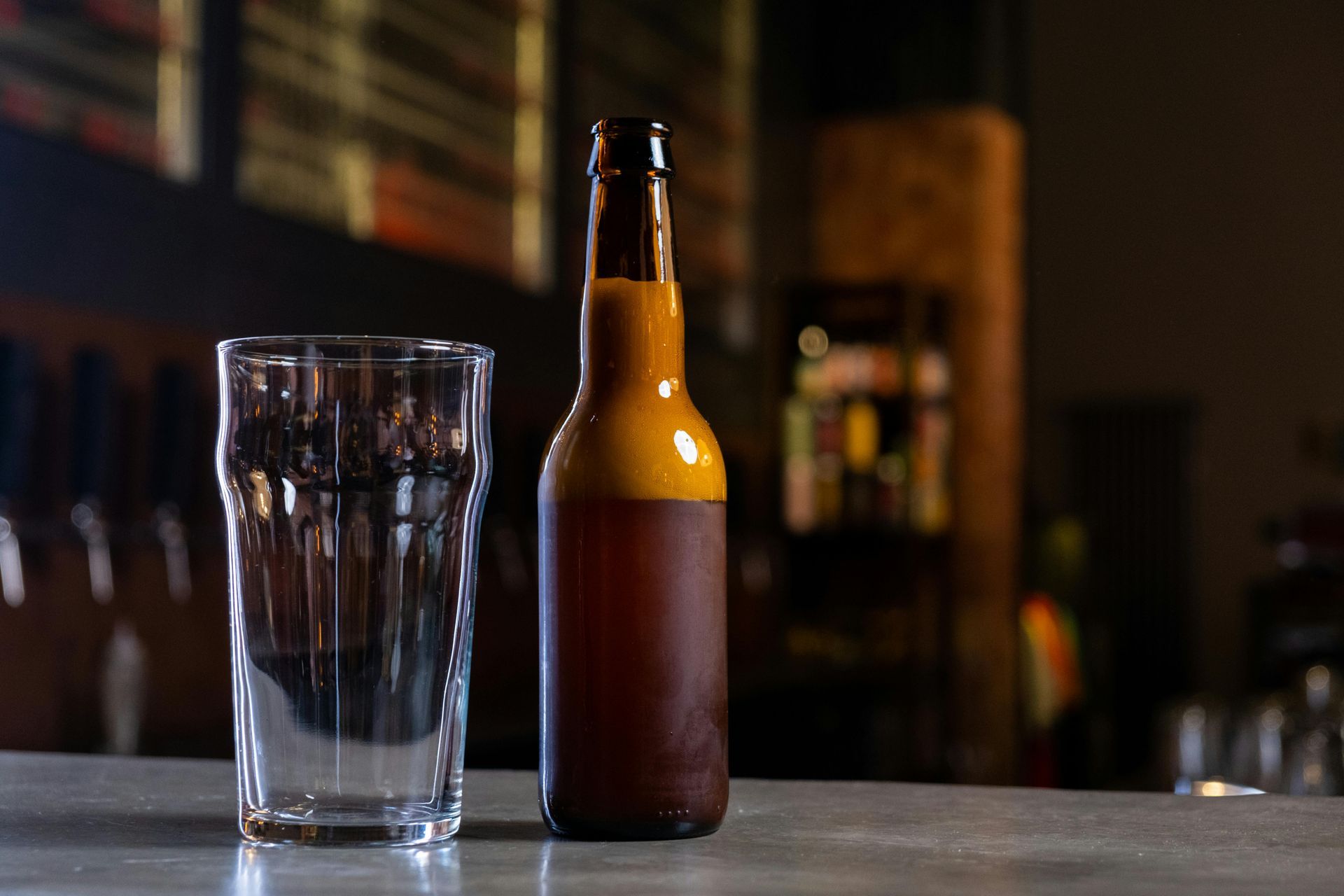 Vaso vacío junto a una botella de cerveza marrón en la barra.