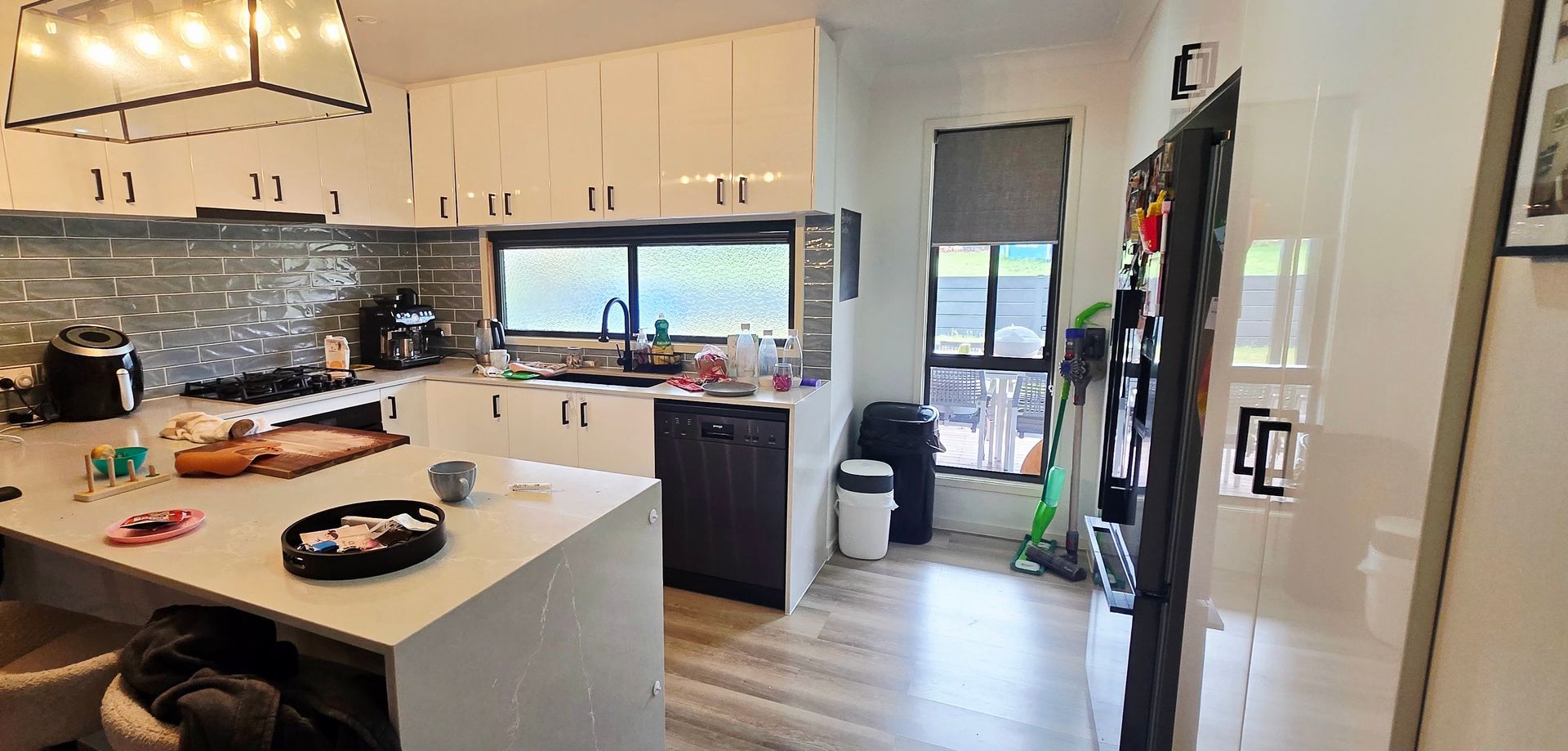 Modern kitchen with island, white cabinets, stainless fridge, and large window under pendant lights