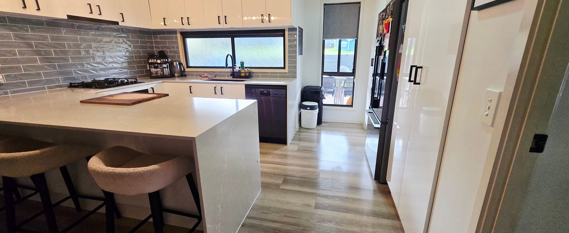 Modern kitchen with white island, bar stools, tiled backsplash, and wood flooring