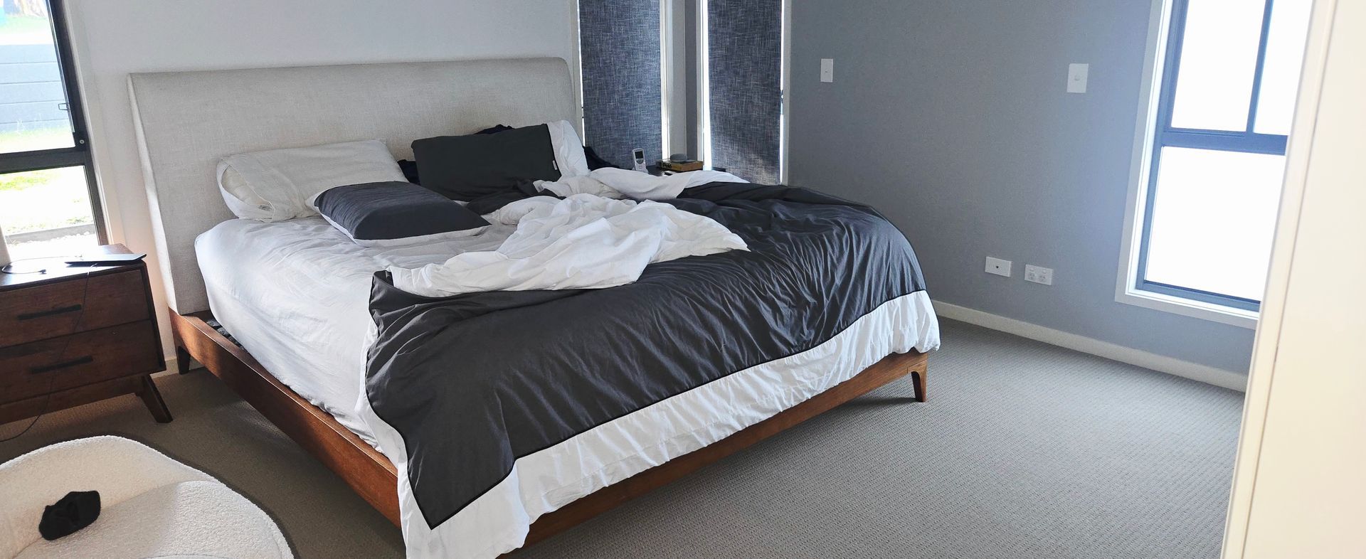 Neatly made bedroom with a bed, nightstand, and a large window on the right