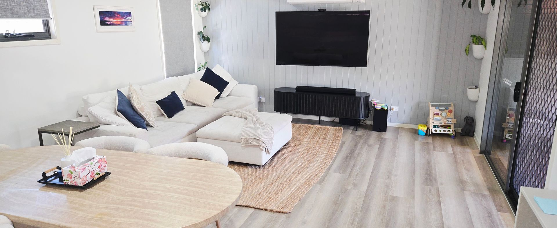 Modern living room with white sectional sofa, wall-mounted TV, round coffee table, and light wood flooring cleaned by Elite care and clean.