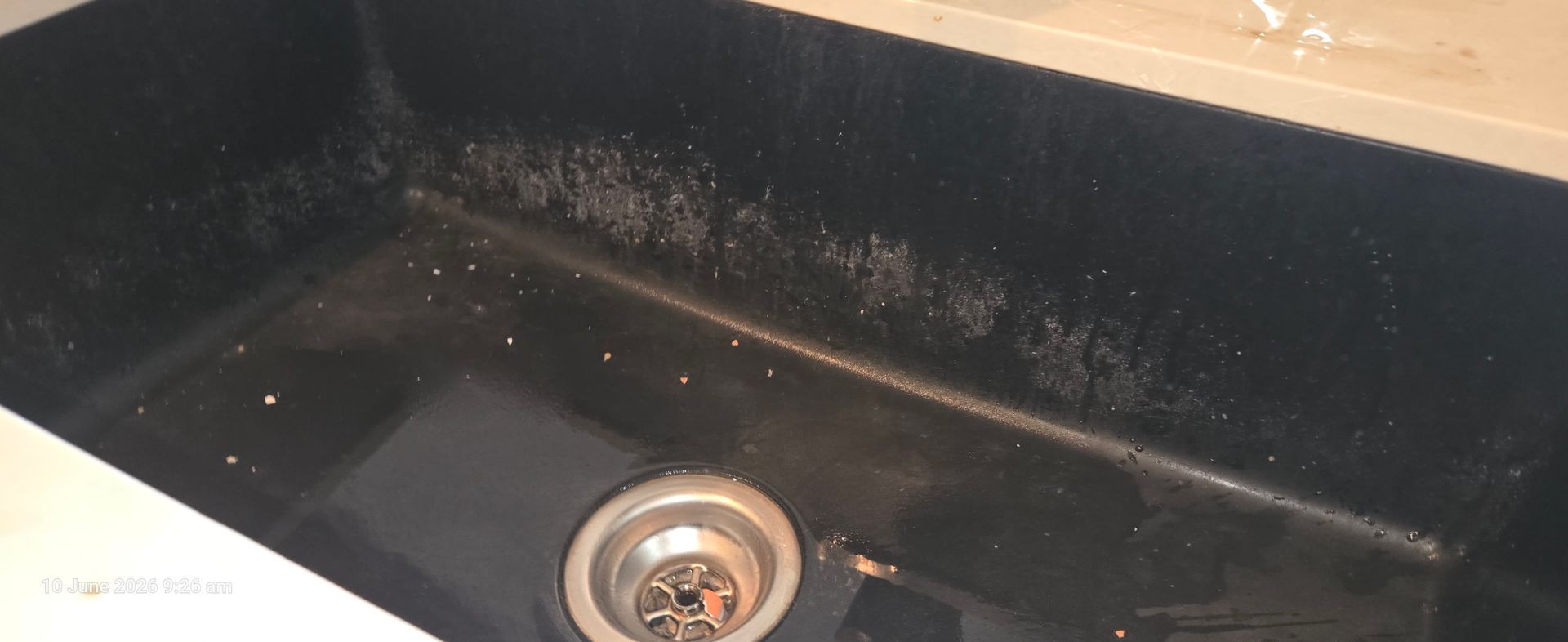 Black kitchen sink with a shiny metal drain and a wooden counter edge above it.